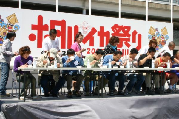 ステージ上でホタルイカの大食いコンテストをしている参加者の写真