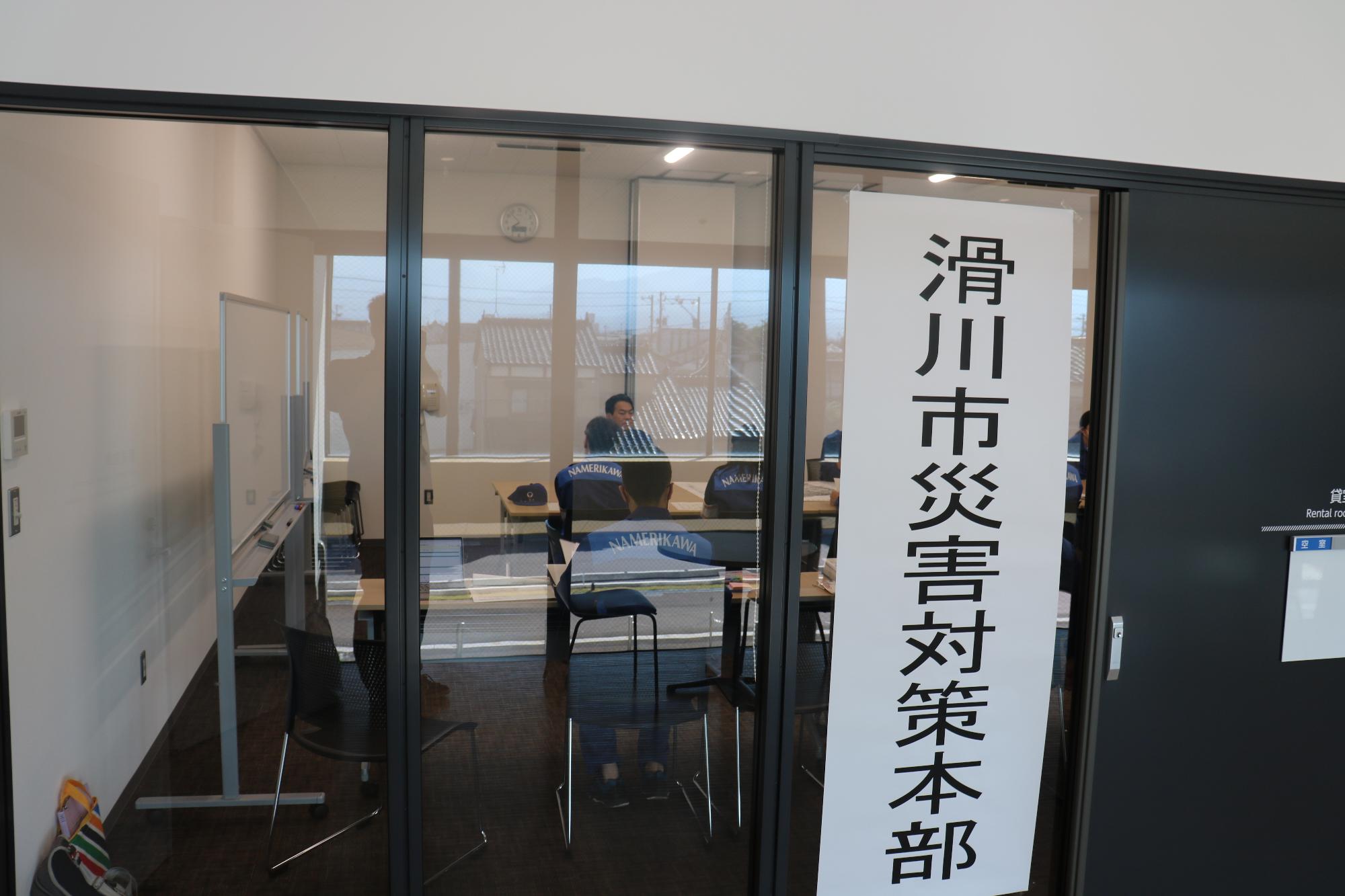 滑川市災害対策本部と書かれた紙が掲示され、ガラス越しに中で会議が行われている様子の写真