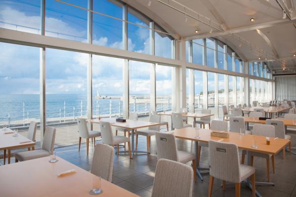 レストランの中にたくさんのテーブルと椅子が並んでいて、全面ガラス張りの窓の外には海が見えている写真