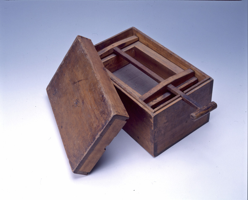 木製の箱型で、蓋がついており、箱の中に柄のついた道具が納められている絹ぶるいの写真