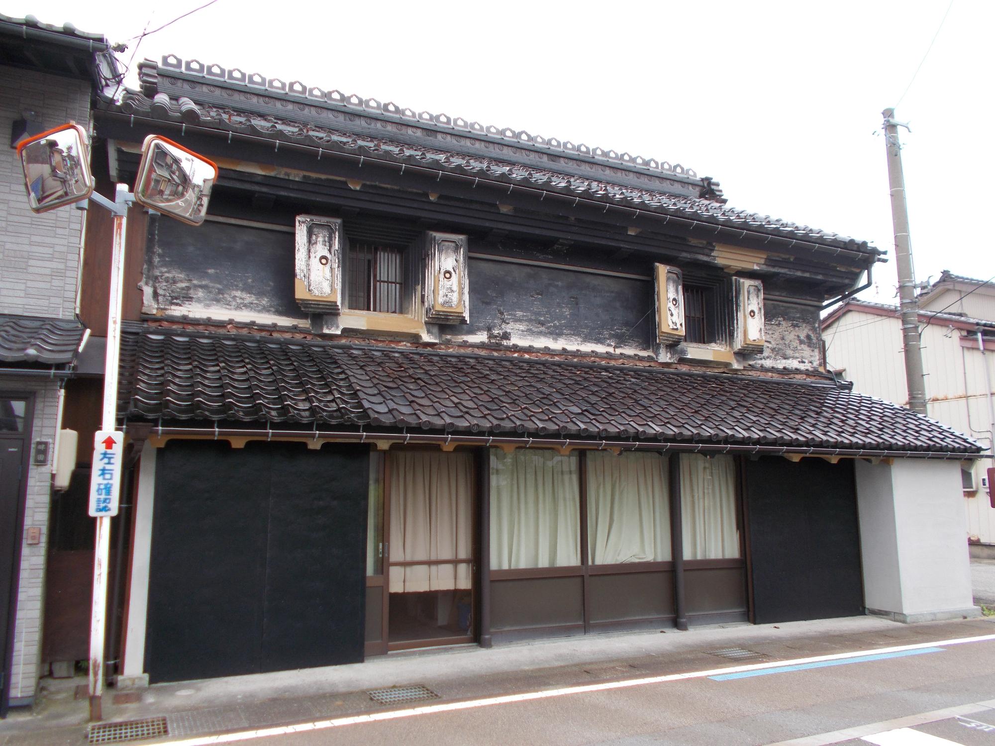 横長の2階建て、黒漆喰で塗られた小沢家住宅店蔵の外観写真