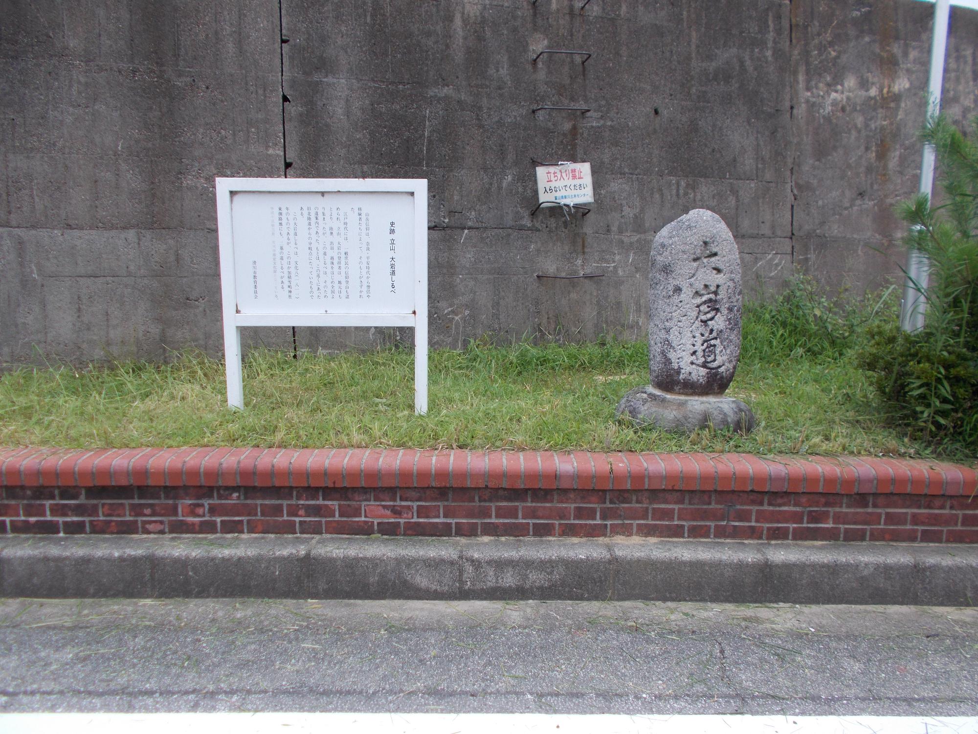 楕円形の岩に「大岩道」と刻まれた「大岩道しるべ」と横に白い案内板が設置設置されている写真