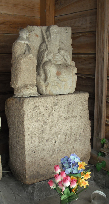 お花が供えられ、2人の人物が彫られた石像と下の台座には「大岩道 是ヨリ四里」の文字が刻まれた石像の台座写真