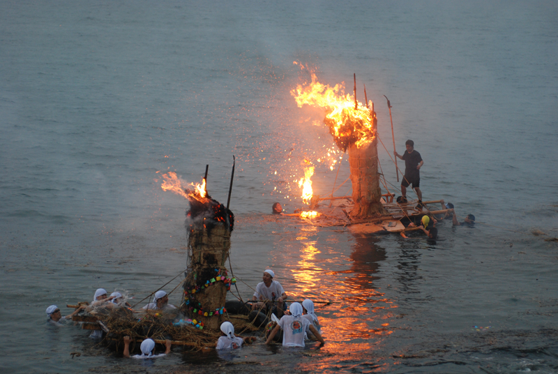 人形（ひとがた）を飾り付け点火された筏2枚が海上に浮かんでいる滑川のネブタ流しの様子の写真