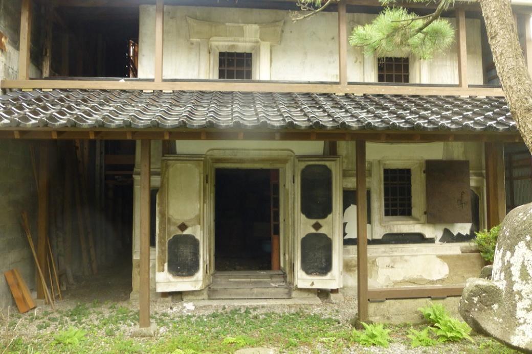 白い外壁の建物で、入口上部に瓦屋根があり、観音開きの扉が設置された菅田家住宅衣装蔵の外観写真
