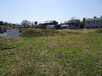 遠くには建物が見え、広々とした草地に白い案内板が立っている東金屋たたら製鉄場跡の写真