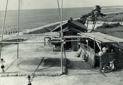 浜辺に1軒の家と倉庫のような建物、土俵がある和田の浜の白黒写真