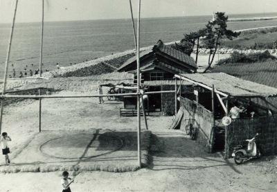 浜辺に1軒の家と倉庫のような建物、土俵がある和田の浜の白黒写真